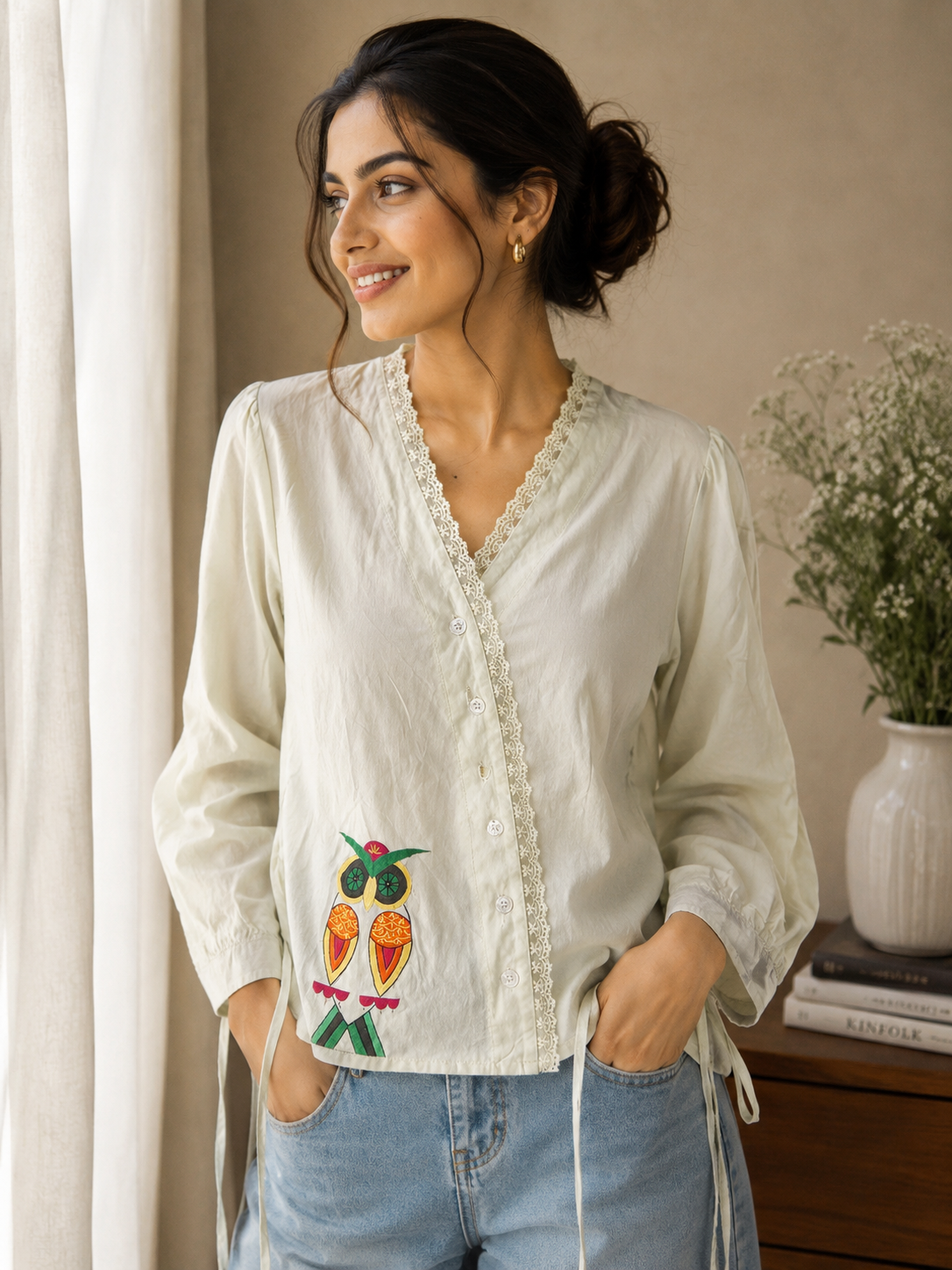 Woman wearing a white embroidered blouse and blue jeans indoors.