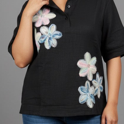 Woman wearing a black polo shirt with floral designs and blue jeans on a gray background