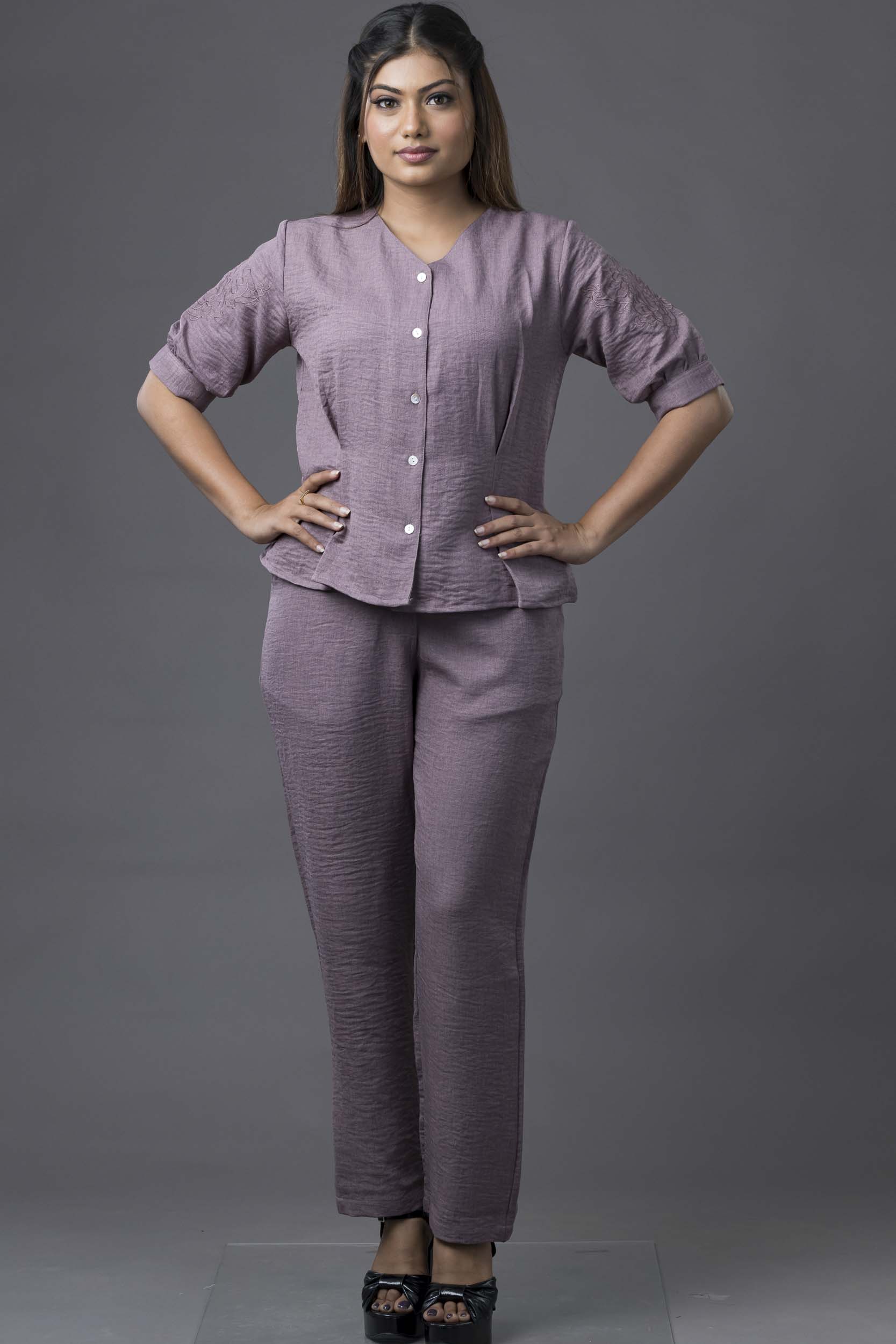 Woman wearing a matching purple outfit with a top and pants on a gray background