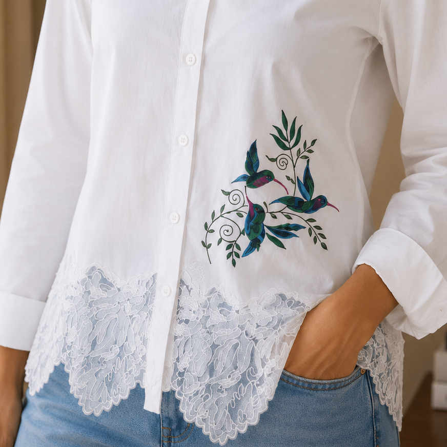 Woman wearing a white blouse with floral embroidery and lace details, standing against a neutral background.